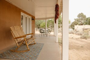 Une véranda couverte avec deux fauteuils à bascule en bois, un tapis à motifs et une décoration suspendue.