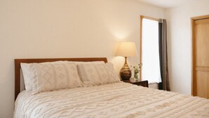 Een bed met een houten hoofdbord, een bedlampje en een spiegel aan de muur.