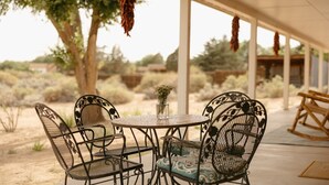 Een terras buiten met een ronde tafel en vier stoelen, omgeven door een overdekt gebied met hangende decoraties.
