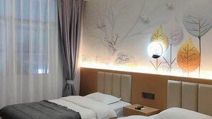 Habitación de hotel con dos camas, cabecera con lámpara y un mural de árboles y hojas en la pared.
