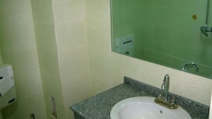 Un baño con lavamanos, espejo y paredes con azulejos verdes.