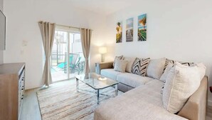 Een moderne woonkamer met een bank, een glazen salontafel en een lamp. Er is een schuifdeur van glas die leidt naar een buitenruimte.
