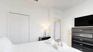 Een moderne hotelkamer met een groot bed, een flatscreen televisie, een kledingkast en een nachtkastje met een lamp.