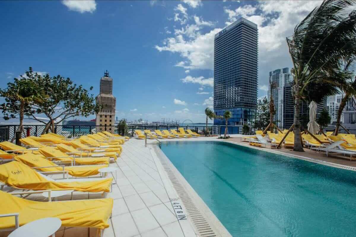 Un espace aménagé au bord de la piscine, avec des chaises longues et une vue dégagée sur un grand immeuble en arrière-plan.