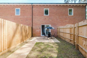 A brick building with a wooden fence, a patio with a table and chairs, and a door.