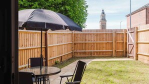 A patio with a table and chairs, a wooden fence, and a clock tower in the background. - Spacious 3 Bed Home With 2 Living Areas & Sofa Bed (Northampton)