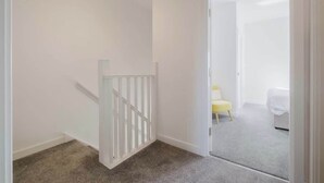 A room with a white door leading to a bedroom with a bed and a yellow chair. - Spacious 3 Bed Home With 2 Living Areas & Sofa Bed (Northampton)