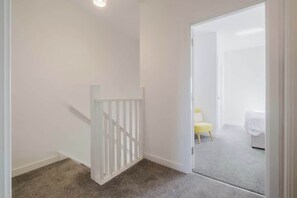 Una habitación con una puerta blanca que da a un dormitorio con una cama y una silla amarilla.