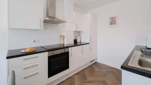 A modern kitchen with white cabinets, a black countertop, and a stainless steel sink. - Spacious 3 Bed Home With 2 Living Areas & Sofa Bed (Northampton)