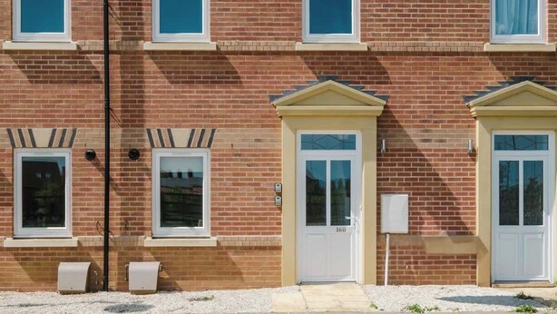 A multi-story brick building with two doors, windows, and a utility box. - Spacious 3 Bed Home With 2 Living Areas & Sofa Bed (Northampton)