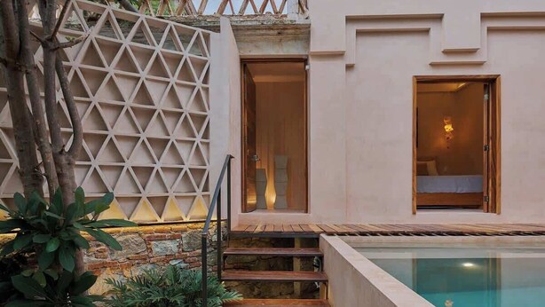 Un espace aménagé au bord de la piscine, avec une terrasse en bois, un escalier menant à une porte et un mur en treillis.