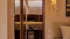 Un couloir étroit mène à une cuisine avec un mur en pierre, une porte en bois et un luminaire suspendu.