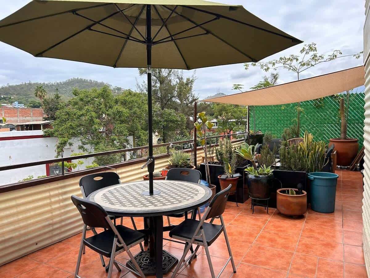 A patio with a round table and chairs, an umbrella, and potted plants.