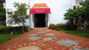 A pathway leading to a building with a red awning and a tiled entrance.