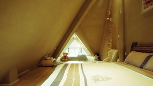 Une chambre confortable située dans les combles, avec un plafond en pente, un grand lit avec une literie à rayures, une chaise et un ours en peluche.