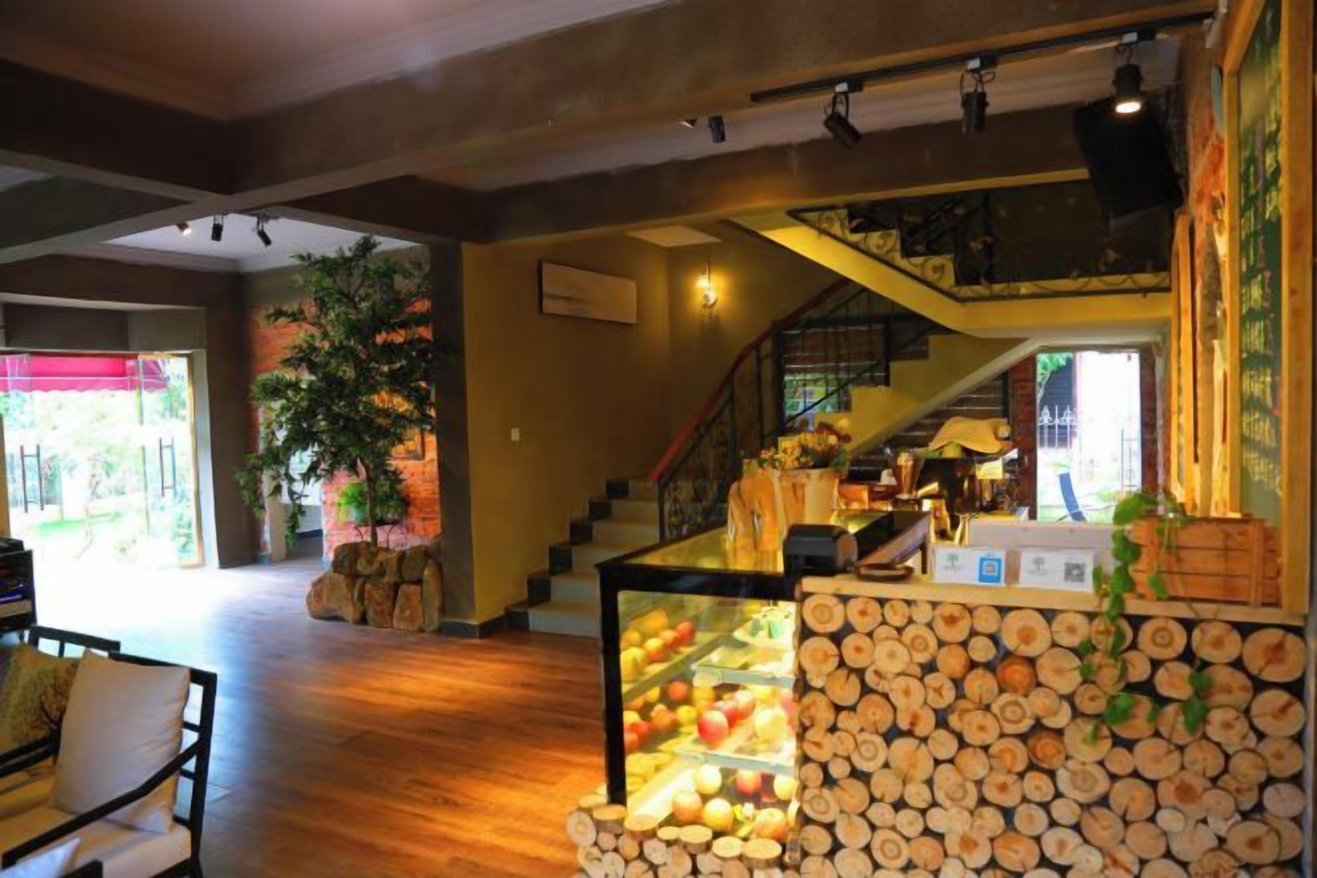 Rebedor d'hotel amb una escala, terres de fusta, una vitrina de vidre amb fruites i una gran planta.
