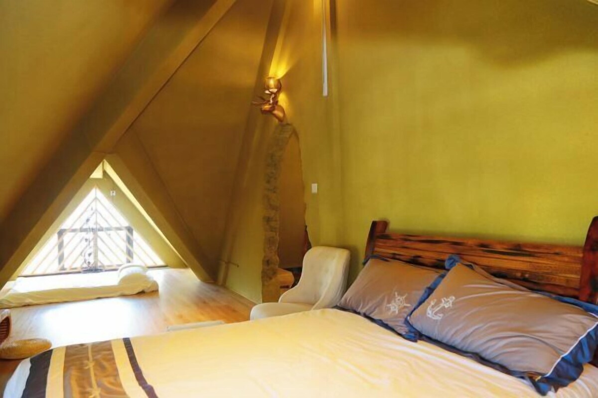 Une chambre avec un plafond en pente, un lit avec des oreillers, une chaise et une fenêtre.
