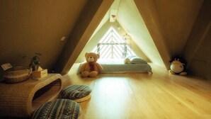 Une chambre mansardée chaleureuse, avec un plafond en pente, une grande fenêtre, un ours en peluche, un pingouin en peluche et un petit lit.