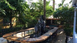 Une terrasse en bois agrémentée d’un élément décoratif central en pierre, entourée d’une végétation luxuriante et d’une piscine.