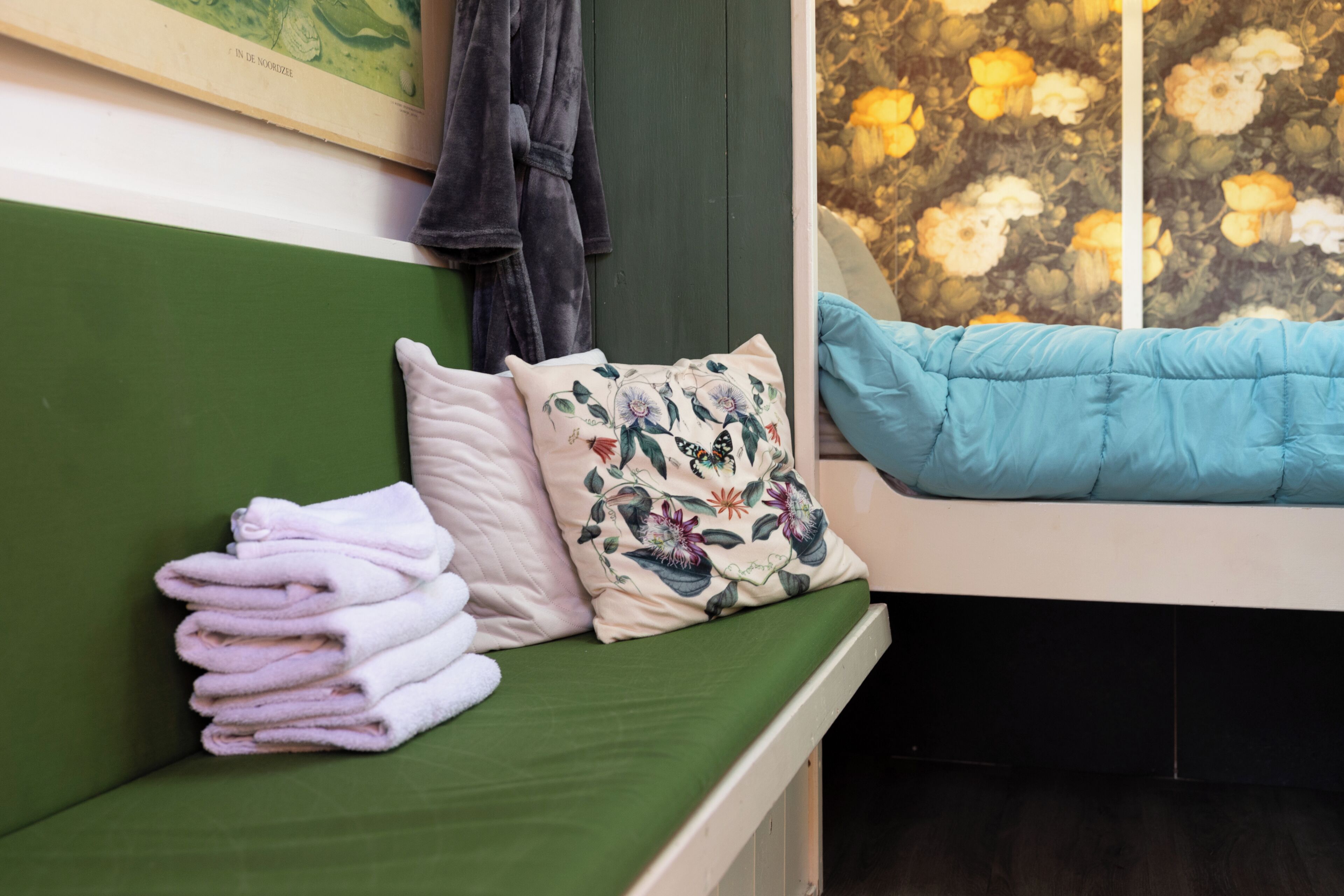 A green bench with a stack of towels, a floral pillow, and a blue cushion.