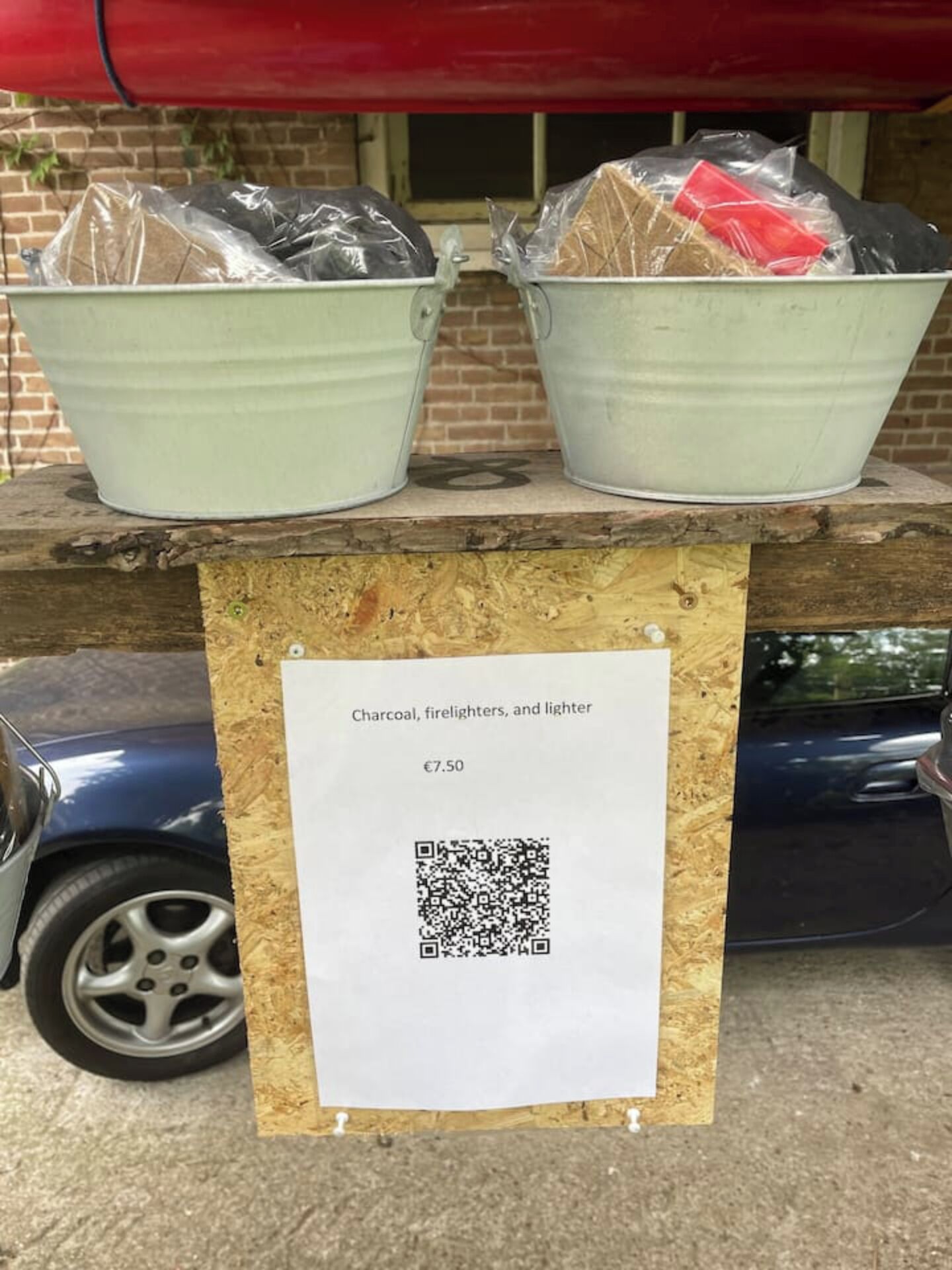 Een houten tafel met twee emmers houtskool, aanmaakblokjes en een aansteker erbovenop, en een prijskaartje van €7,50.