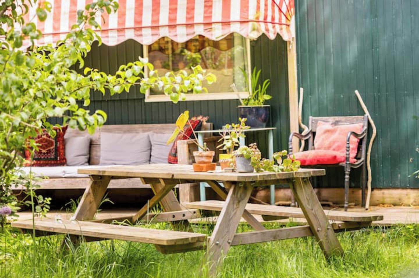Een houten picknicktafel met een bankje, omgeven door groen en potplanten.