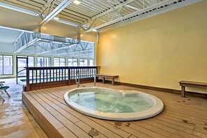 Ein Whirlpool auf einer Holzterrasse mit Metallgeländer, einer Sitzbank und Blick auf einen Pool durch große Fenster.
