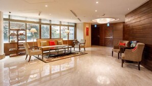 A spacious lobby with a sofa set, armchairs, and a coffee table. Large windows provide natural light and a view of the outdoors.