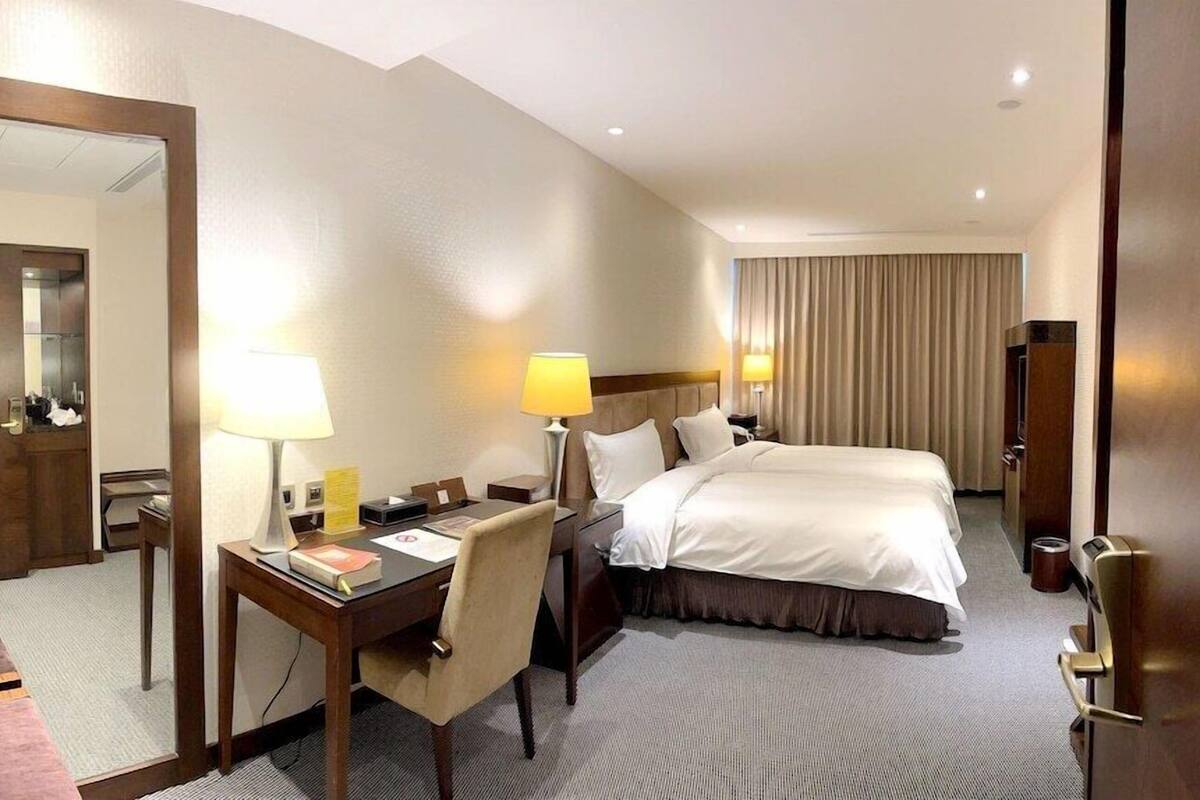 Una habitación de hotel con cama, escritorio, silla, lámparas y espejo.
