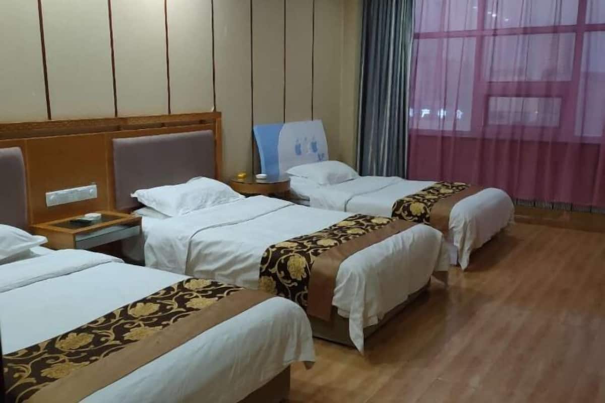 Habitación de hotel con tres camas, cabeceros de madera, un mesita de noche y una ventana con cortinas translúcidas.