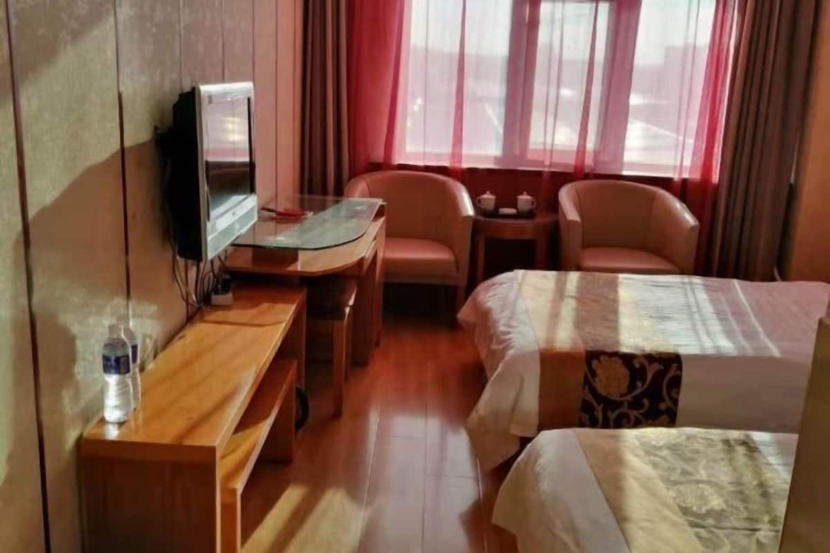 Una habitación de hotel con cama, dos sillas, una mesita, televisor y ventana con cortinas.