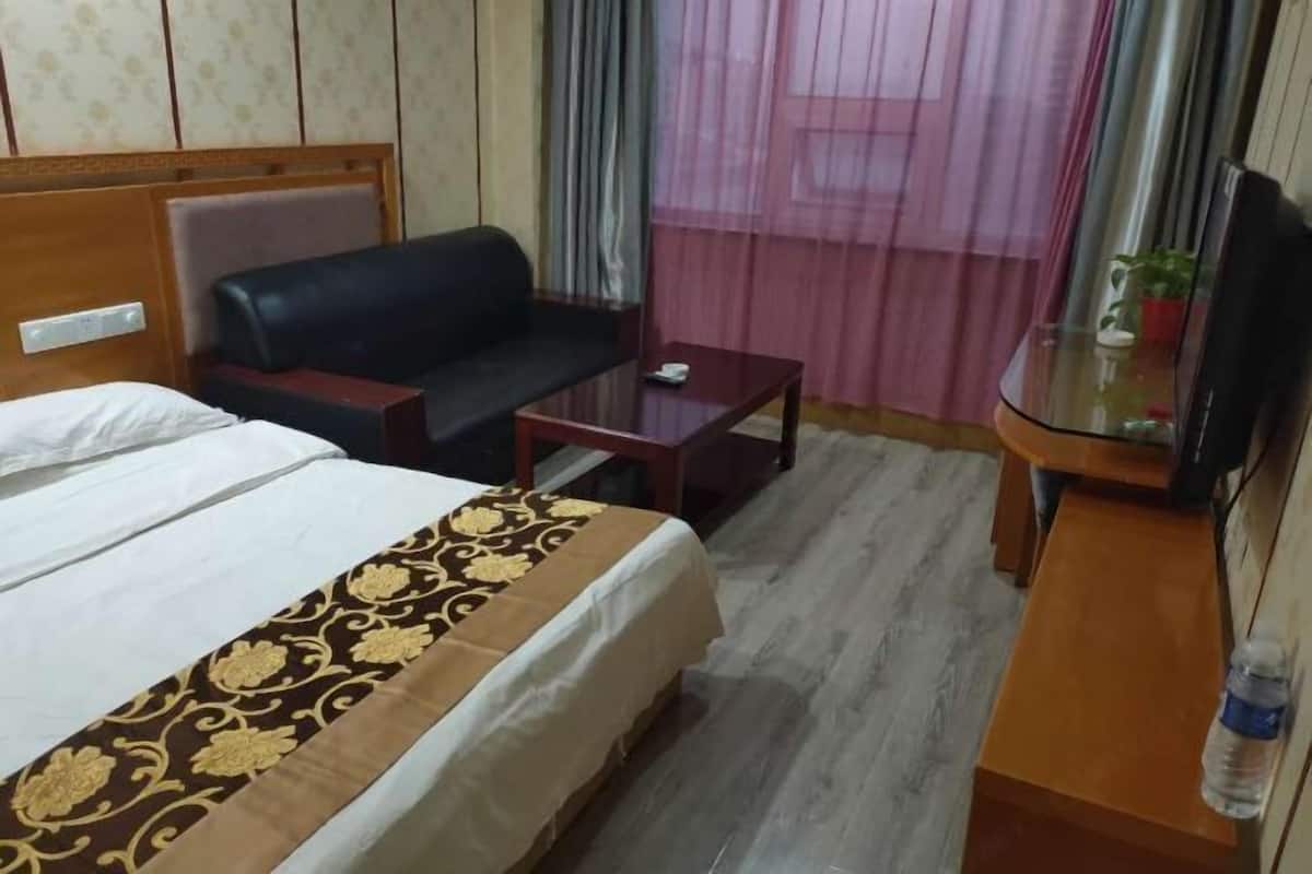 Una habitación de hotel con cama, sofá, una mesita, televisor y ventana con cortinas.