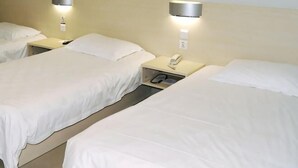 Una habitación de hotel con tres camas individuales, cada una con una mesita de noche y lámpara.