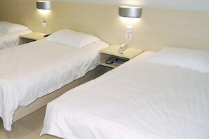 Una habitación de hotel con tres camas individuales, cada una con una mesita de noche y lámpara.