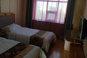 Ein Hotelzimmer mit zwei Betten, einem Fernseher und einem Fenster mit Vorhängen.