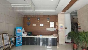 Zona de recepción con un mostrador de madera, un quiosco informativo azul y una escalera a la derecha.