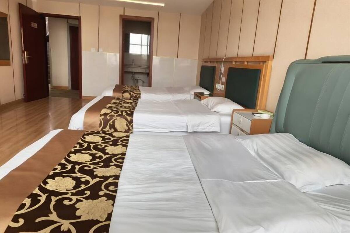 Habitación de hotel con dos camas, piso de madera, alfombra estampada y vista al pasillo.