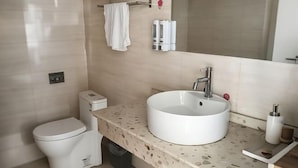 Un baño moderno con un lavamanos blanco, un inodoro, un perchero para toallas y un espejo.