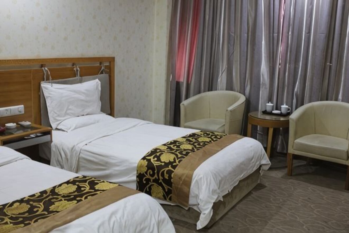 Une chambre d’hôtel avec deux lits, une tête de lit en bois, une petite table avec des tasses et une chaise.