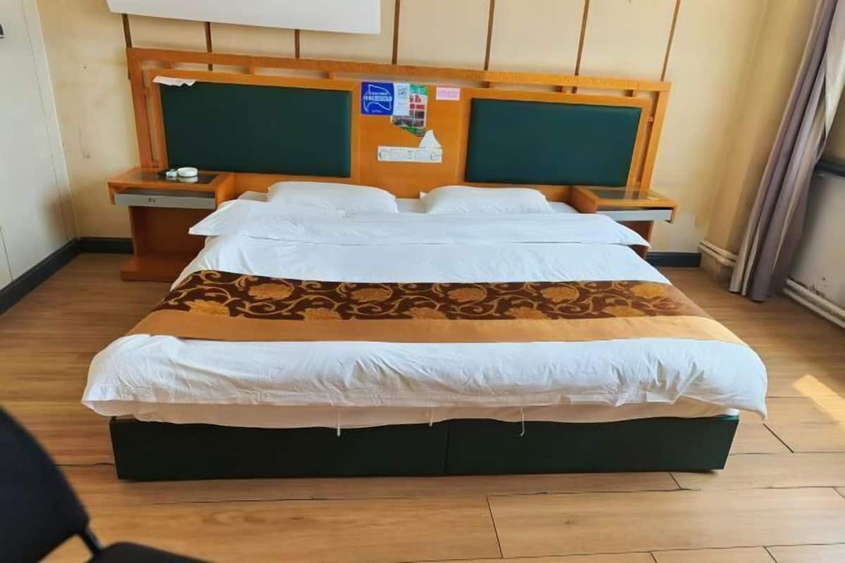 Una habitación de hotel con una cama grande, cabecero de madera, dos mesitas de noche y una pared verde.