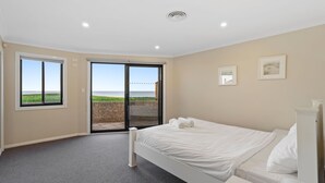 Un dormitorio con cama, ventana grande y puerta corrediza de vidrio que da a un balcón con vista al mar.