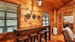 A wooden cabin interior with a bar area, three stools, a white trash can, and a chair. - Immersive Forest Experience (Ellijay)