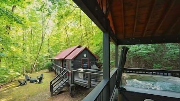 A cabin with a wooden deck and a hot tub, surrounded by dense forest. - Immersive Forest Experience (Ellijay)