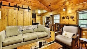 A cozy cabin interior with a wooden ceiling, a sofa, a chair, and a small table. - Immersive Forest Experience (Ellijay)