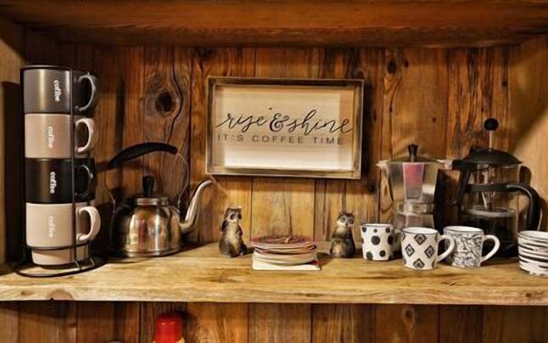 Une étagère en bois sur laquelle sont disposés divers ustensiles pour préparer le café et des tasses, notamment une cafetière à piston, une cafetière classique et un panneau indiquant : « C’est l’heure du café. »
