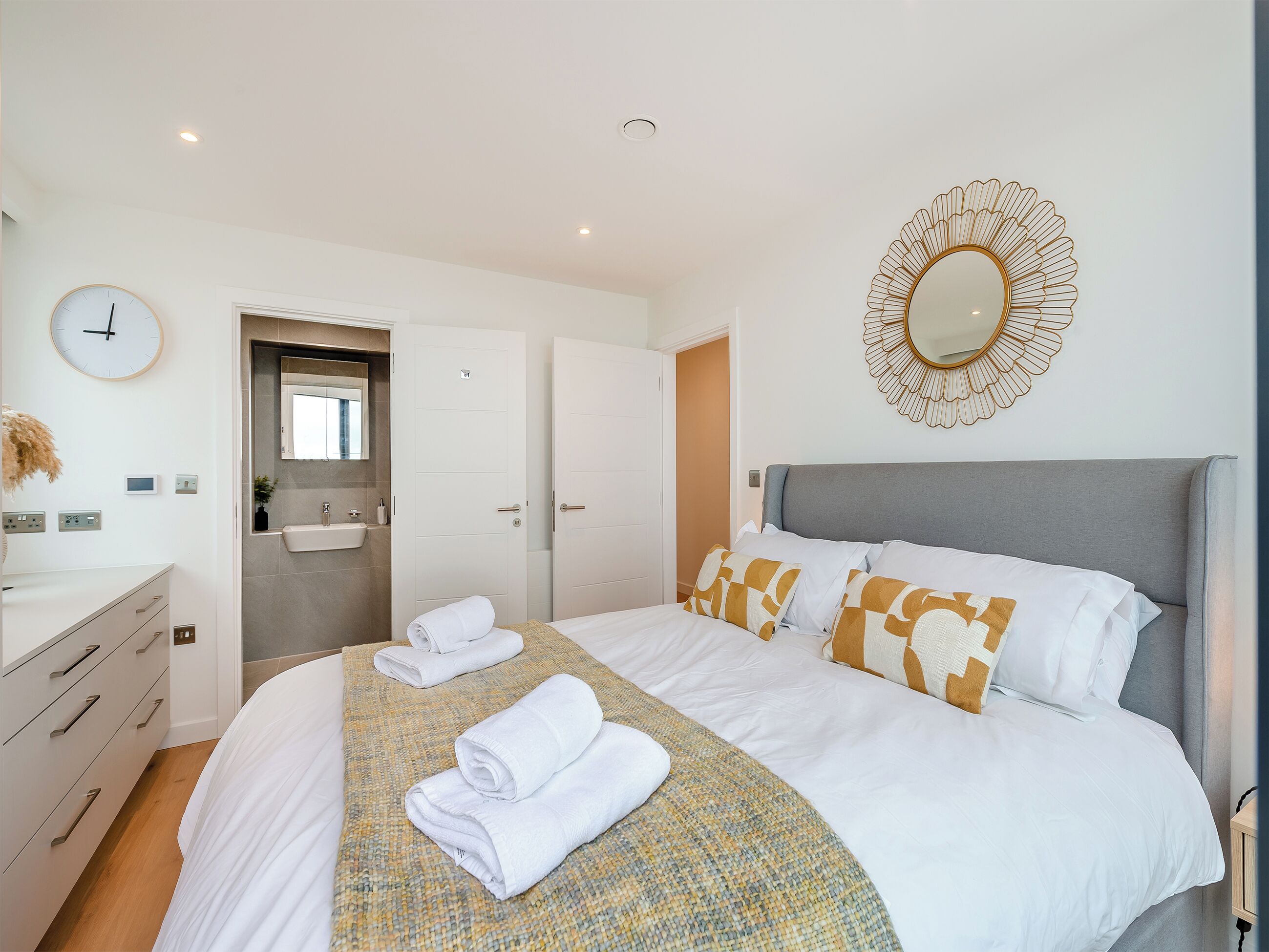A hotel room with a bed, a bedside table, a mirror, and a clock.