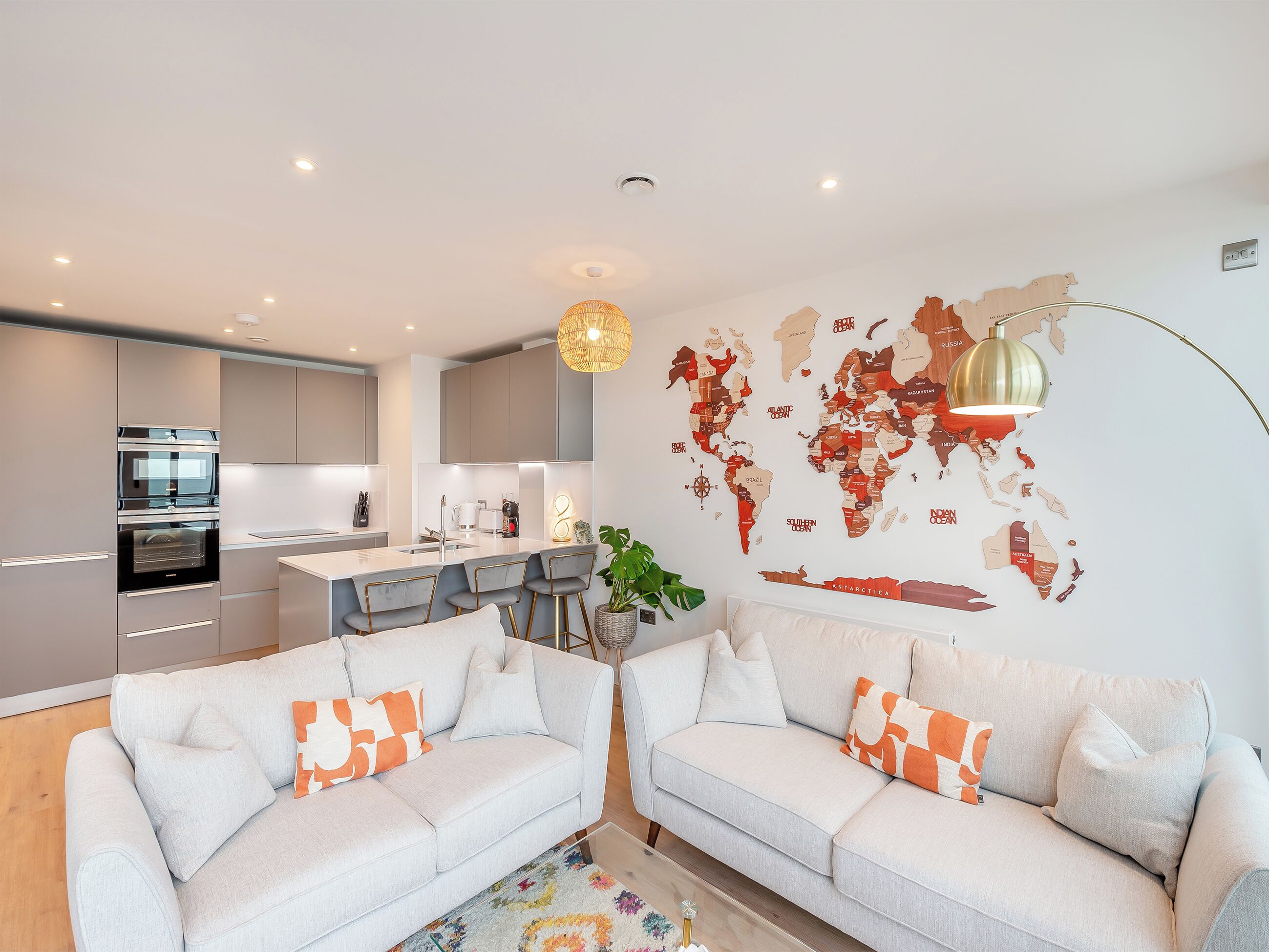 A modern apartment with a kitchen, two sofas, a world map wall, and a pendant light.