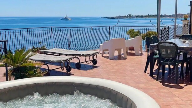 A terrace with a hot tub, lounge chairs, and a table with chairs overlooking a body of water.