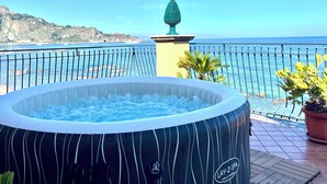 A hot tub on a terrace with a view of the sea and a rocky coastline.