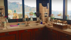 A kitchen with a view of a coastal landscape, featuring a sink, cabinets, and various kitchen utensils.